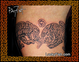 Tattoo of two battling Pictish animals on a person's arm with 'Lucky Fish' branding.
