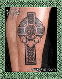 Celtic cross tattoo with claddagh and heart on a person's leg with Lucky Fish branding.