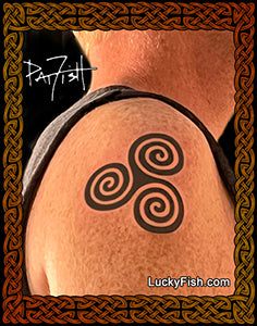 Tattoo of a triskele symbol on skin with 'Lucky Fish' branding.