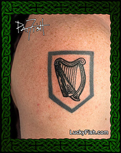 Tattoo of an Irish harp design on skin with 'Lucky Fish' branding.