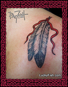 Tattoo of an eagle feather with red ribbon on skin, framed with Celtic knotwork and 'LuckyFish.com' branding.