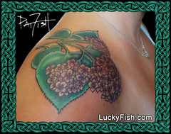 Tattoo of purple hydrangea flowers and green leaves by Pat Fish on a person's shoulder with LuckyFish branding.