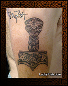 Tattoo of a Viking hammer with intricate designs on a person's arm, signed by Lucky Fish.
