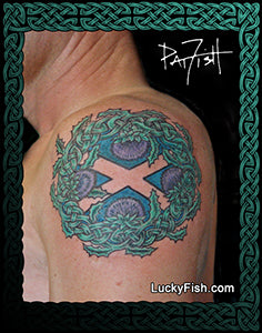 Tattoo of a Celtic Scottish saltire flag cross design with thistles on a person's shoulder with 'Lucky Fish' branding.