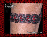 A close-up of a person's arm skin with a black and red Viking knotwork tattoo design across the forearm, framed by a red decorative border with the LuckyFish.com watermark.