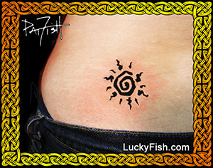 Tattoo of a black spiral sun design on a person's lower back, framed by a decorative gold Celtic knot border with the LuckyFish.com logo.