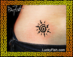 Tattoo of a black spiral sun design on a person's lower back, framed by a decorative gold Celtic knot border with the LuckyFish.com logo.