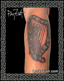 Tattoo of a Celtic harp design on a person's arm with 'Lucky Fish' branding.