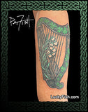 Tattoo of a green harp with flowers on a person's arm with Celtic knotwork and 'LuckyFish.com' branding
