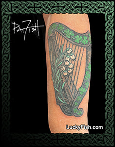 Tattoo of a green harp with flowers on a person's arm with Celtic knotwork and 'LuckyFish.com' branding