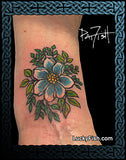 Tattoo of a blue flower with green leaves on a person's arm, artist 'Lucky Fish' visible.