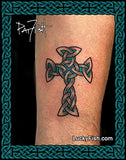 A tattoo of a Celtic cross with black and teal-green line art on human skin, framed by a decorative teal border with the LuckyFish.com logo and artist signature.