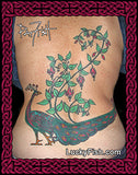 Tattoo of a peacock with fuchsia floral elements on a person's back, featuring the brand 'Lucky Fish'.
