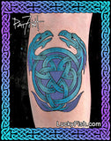 A tattoo design on skin showing two blue-green dragons wrapping around a Celtic knot triquetra and triple triangle symbol, with a purple and blue Celtic border frame and the text LuckyFish.com.