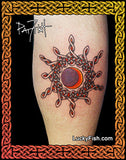 A sunburst tattoo applied to a person's leg, featuring a Celtic knot design with a central red and orange moon surrounded by knotwork. The image is framed by a decorative Celtic border with a black background, and a watermark 'LuckyFish.